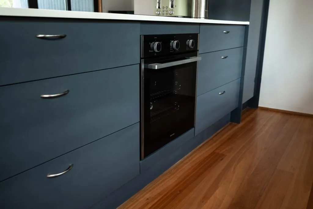 An image of the interior of a modular kitchen, with timber floors and black kitchen drawers