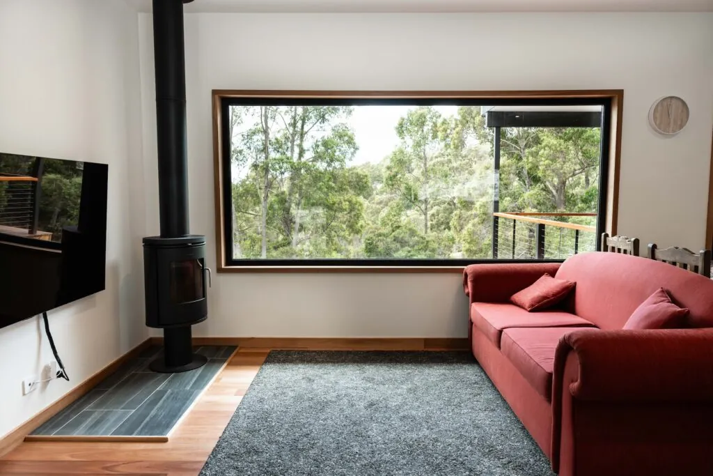 Modular home living room with wood fire heater, tv, red couch, and expansive windows 